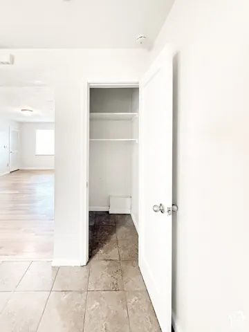 Storage closet with interior shelving, neutral tile flooring, and a traditional hinged door