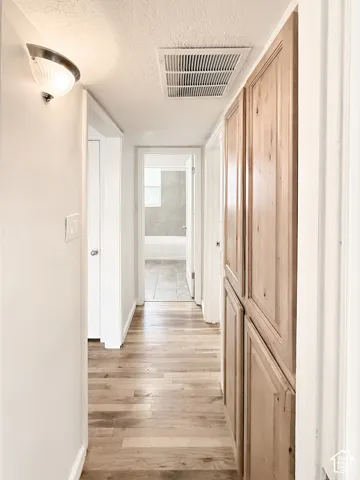 Hallway featuring wood-finish flooring, floor-to-ceiling wooden cabinetry, and wall-mounted lighting