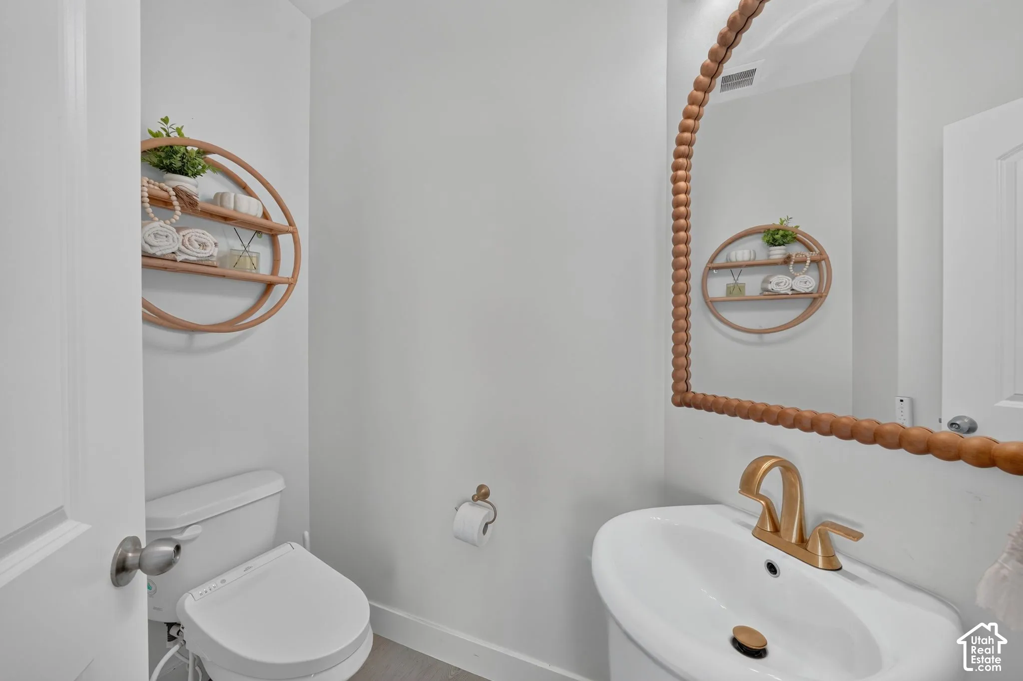 Pedestal sink with brass-toned widespread faucet and matching hardware, arch-top mirror with beaded wood frame, and dual-flush toilet