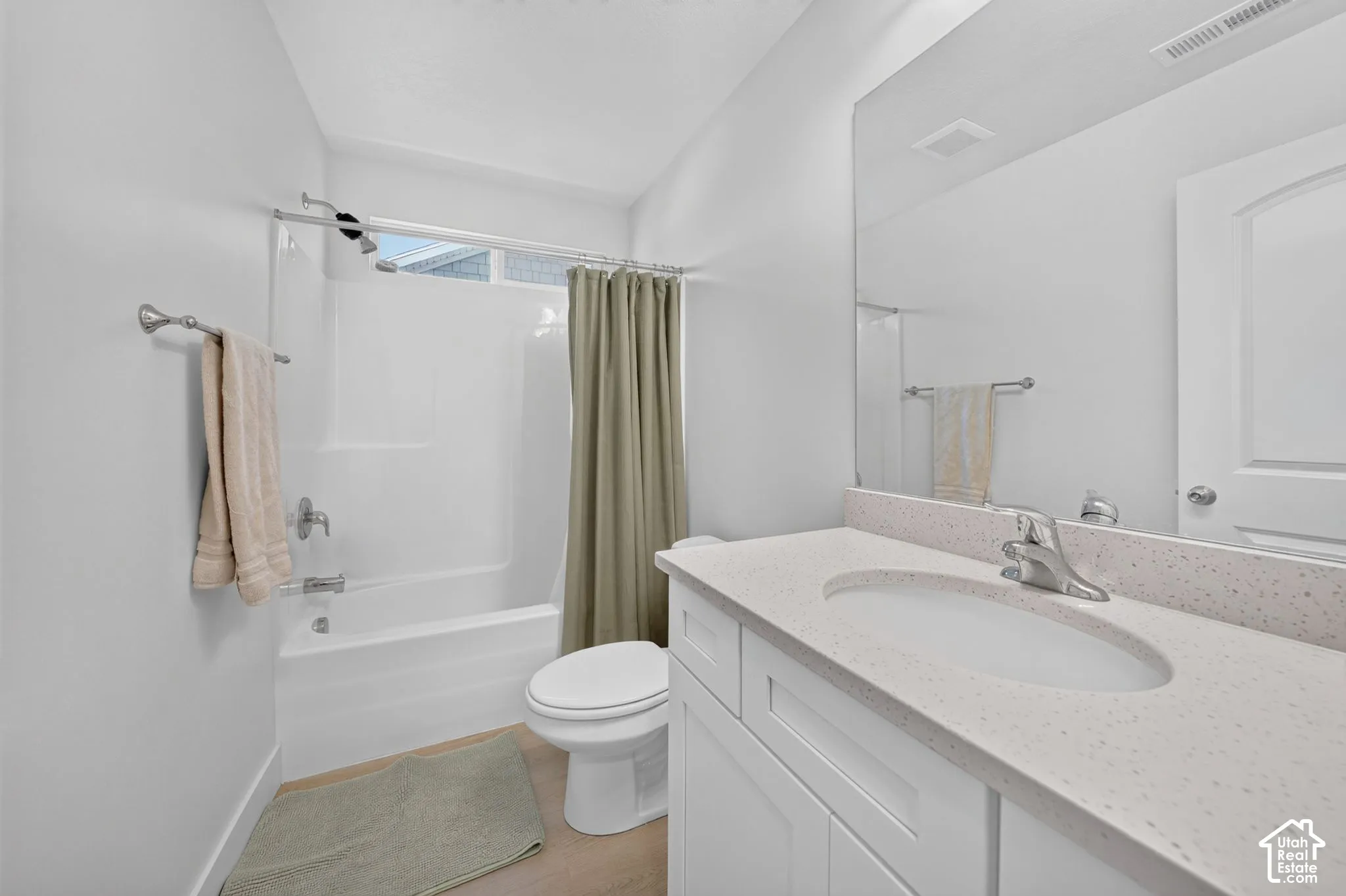 Full-width vanity with solid-surface countertop and integrated sink, large wall-mounted mirror, and combination bathtub-shower enclosure with white surround