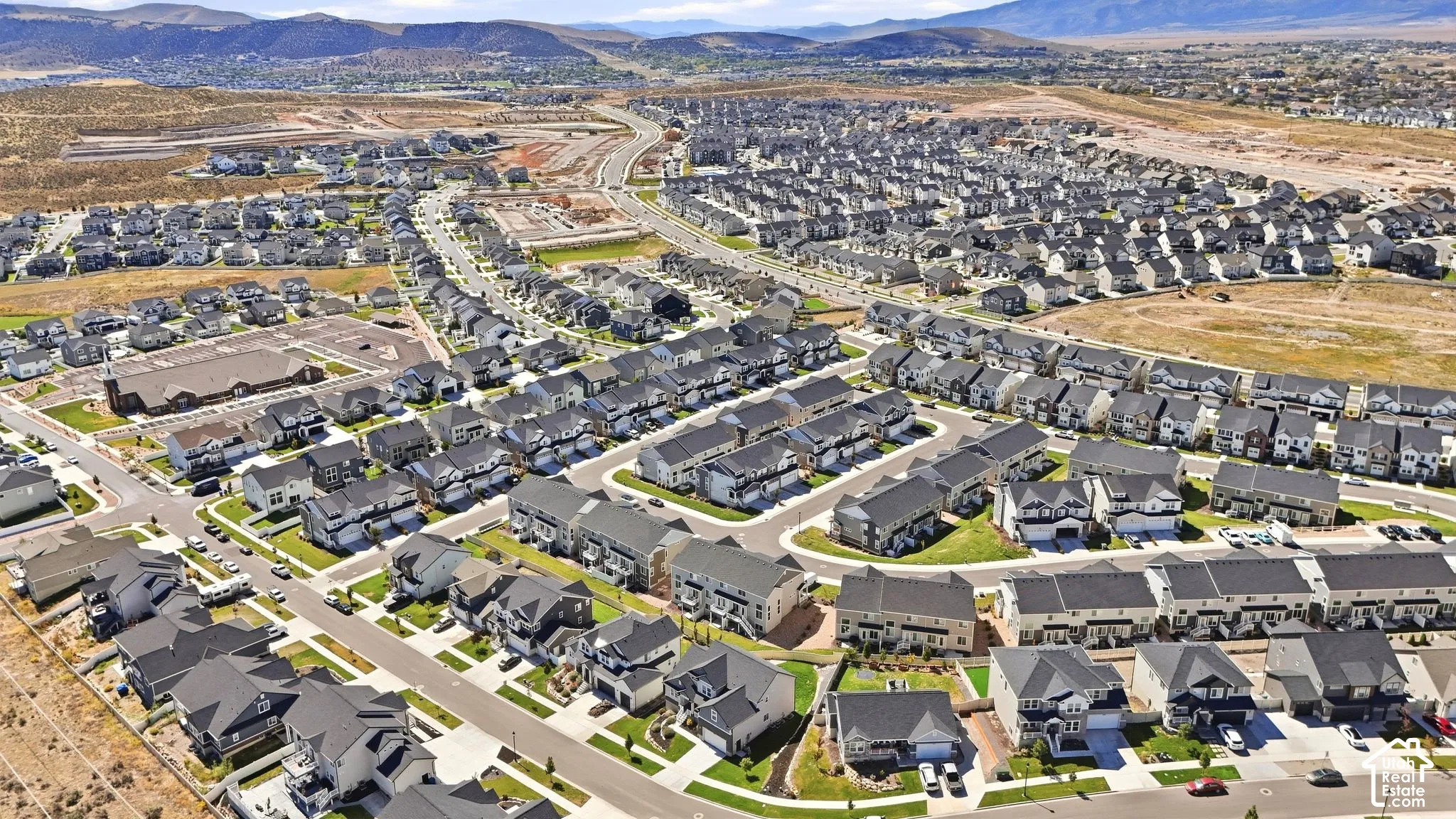Aerial perspective of a planned residential community featuring paved streets, asphalt-shingled roofing, and a mountain range backdrop