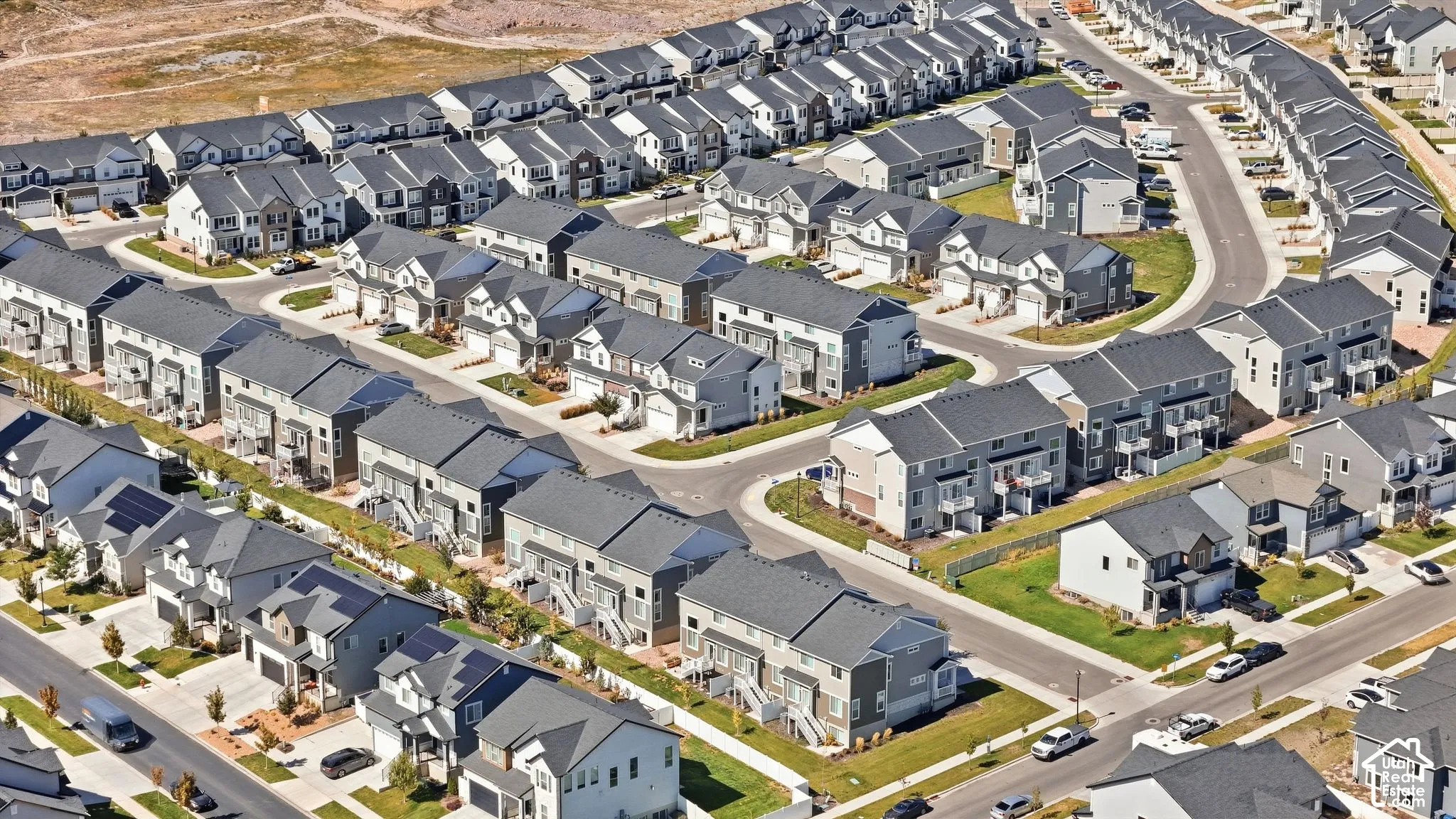 Aerial perspective of a multi-unit residential community featuring gable rooflines, diverse siding materials, paved roadways, and integrated garage structures