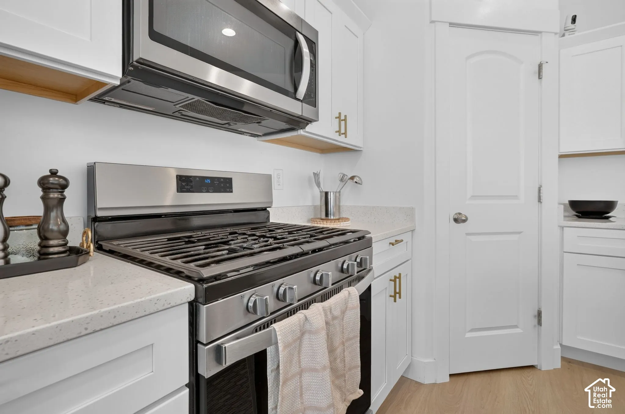 Kitchen featuring white shaker-style cabinetry, quartz countertops, stainless steel gas range, over-the-range microwave, and wood-finish flooring
