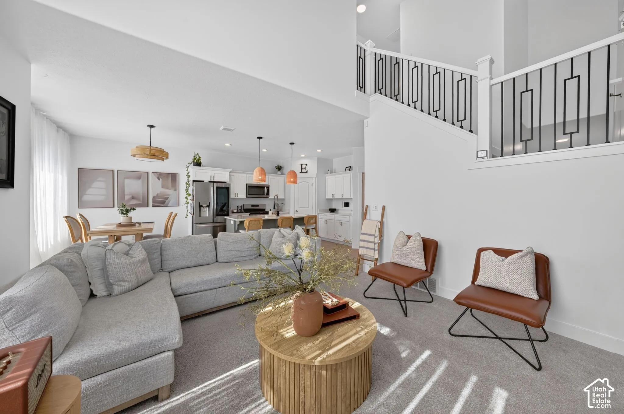 Open-concept interior featuring vaulted ceilings, a kitchen with island seating, pendant lighting, and a staircase with geometric metal balusters