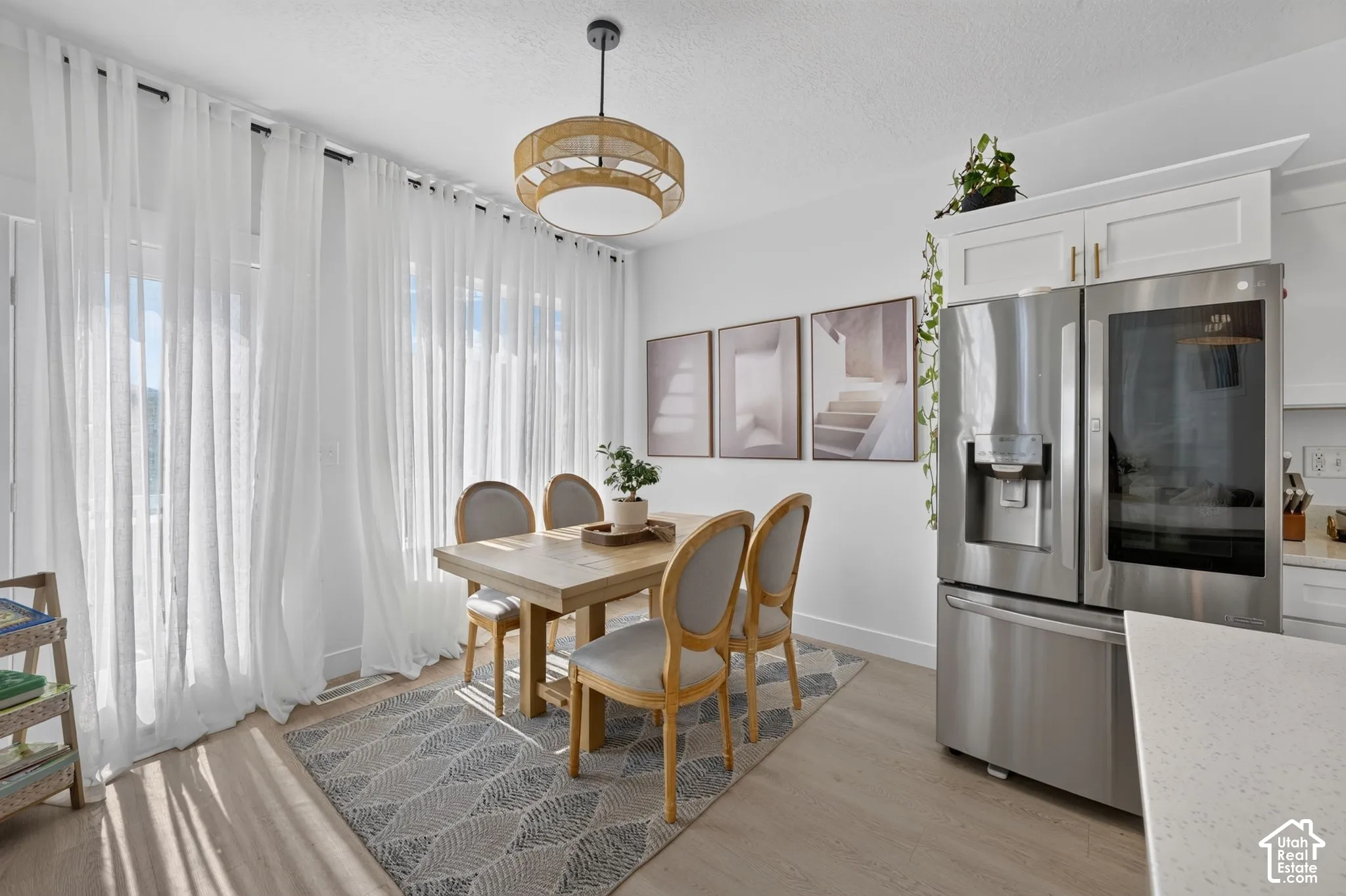 Dining area featuring light-toned flooring, white cabinetry, a stainless steel refrigerator, quartz countertops, and a drum-style pendant light fixture