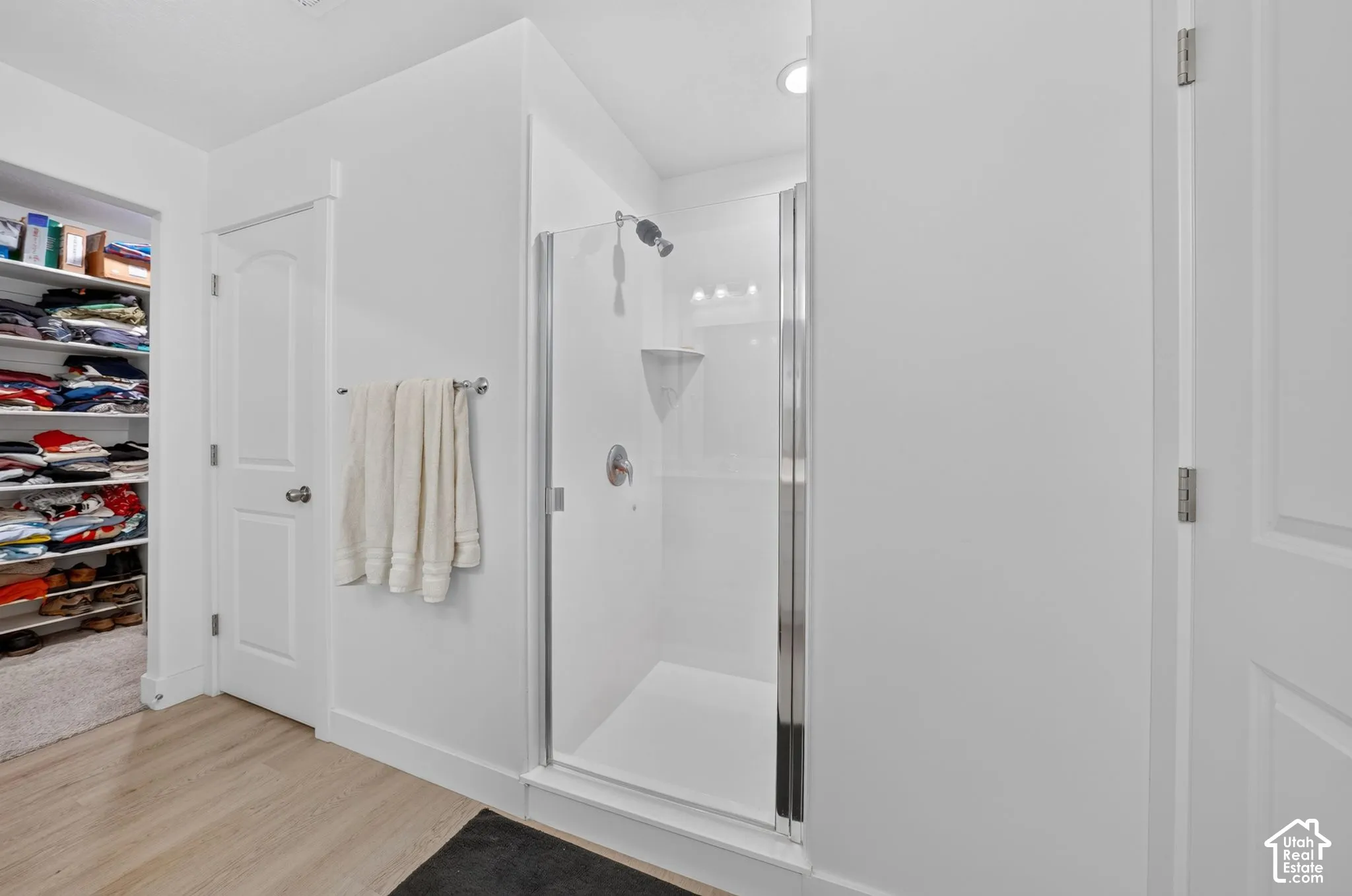 Walk-in shower with a glass enclosure, wood-finish flooring, and recessed lighting