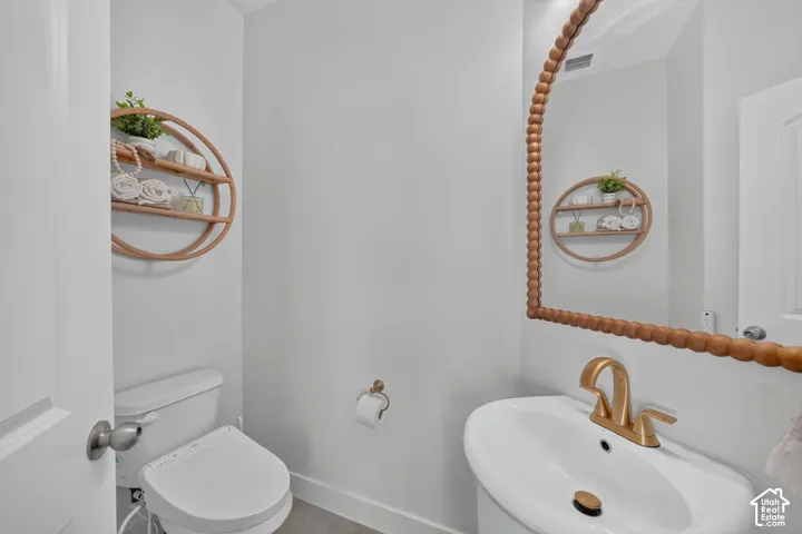 Pedestal sink with brass-toned widespread faucet and matching hardware, arch-top mirror with beaded wood frame, and dual-flush toilet