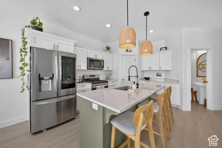 Kitchen featuring white shaker-style cabinetry, stainless steel appliances, a central island with a solid surface countertop, wood-finish flooring, and pendant lighting
