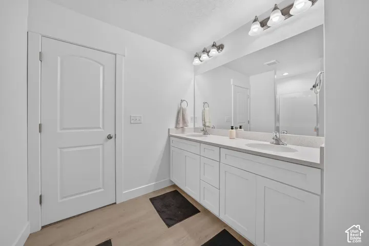Dual-sink vanity with white shaker-style cabinetry, solid-surface countertop, full-width mirror, and two multi-bulb vanity light fixtures over wood-finish flooring