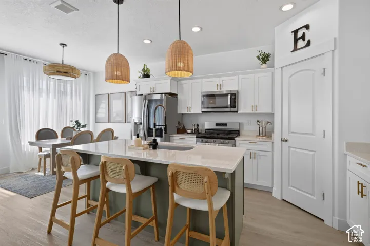 Kitchen featuring a central island with a solid-surface countertop, white shaker-style cabinetry, recessed lighting, woven pendant fixtures, and wood-finish flooring