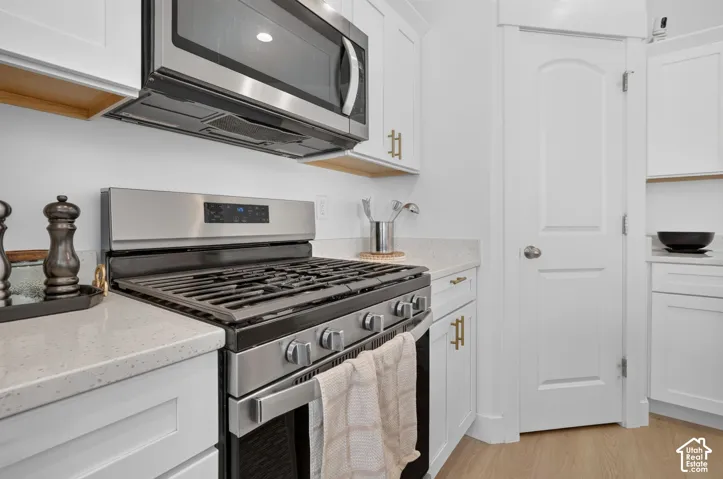 Kitchen featuring white shaker-style cabinetry, quartz countertops, stainless steel gas range, over-the-range microwave, and wood-finish flooring