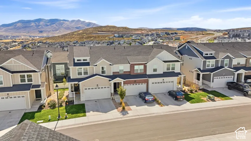 Multi-unit residential exterior featuring mixed siding, brick accents, asphalt shingle roofing, and attached two-car garages, set against a mountainous horizon