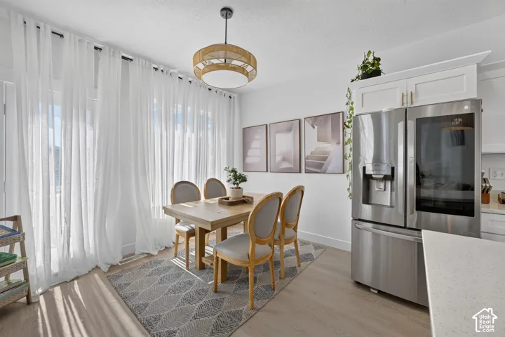 Dining area featuring light-toned flooring, white cabinetry, a stainless steel refrigerator, quartz countertops, and a drum-style pendant light fixture