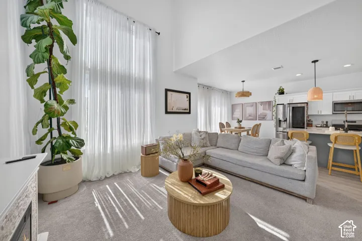 Vaulted ceilings featuring floor-to-ceiling windows, open-concept kitchen with white cabinetry, stainless steel appliances, and dual pendant lighting