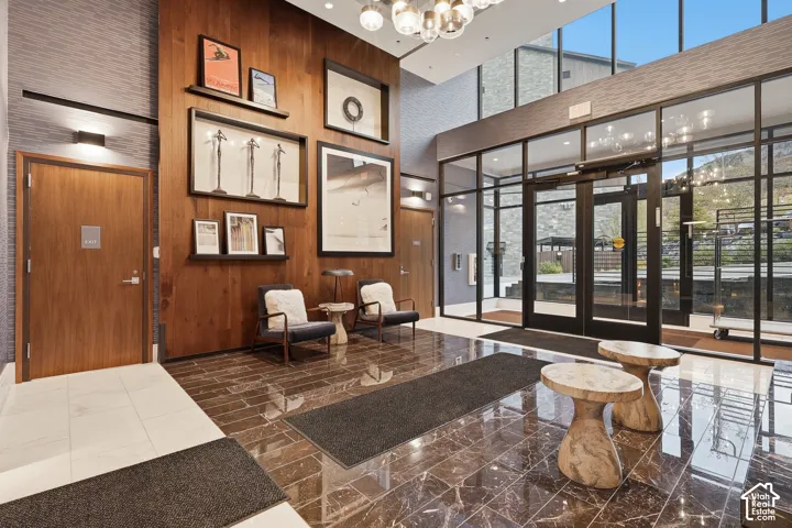 Double-height lobby featuring floor-to-ceiling glass paneling, polished stone flooring, and expansive wood-paneled accent walls