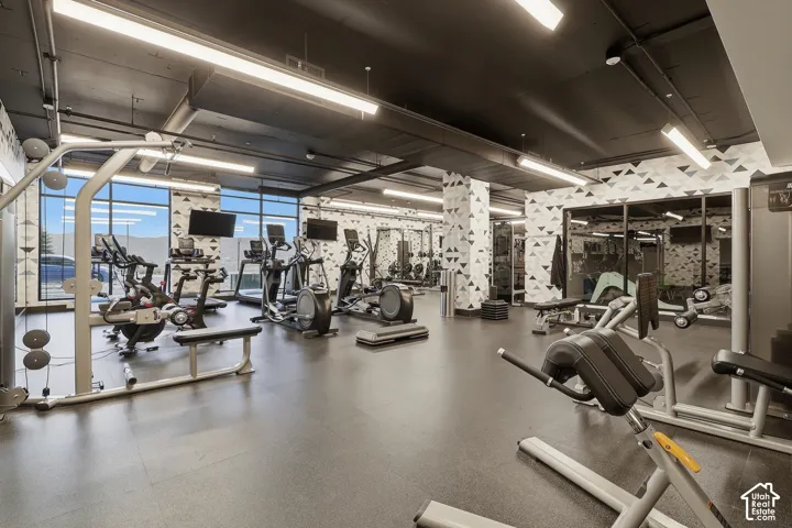Fitness center featuring high ceilings with industrial-style exposed ductwork, large-format floor-to-ceiling windows, mirrored wall panels, and patterned accent walls