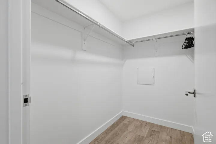 Walk-in closet featuring wood-finish flooring, white shelving, and dual metal clothing rods