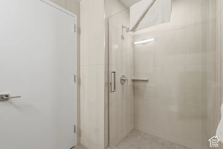 Walk-in shower featuring a frameless glass door, light-toned ceramic wall tile, mosaic tile flooring, a built-in recessed shelf, and polished chrome hardware