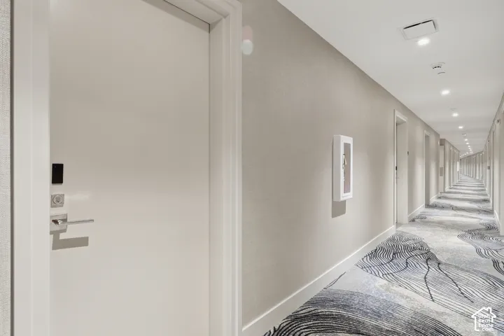 Hallway featuring neutral textured wall coverings, patterned carpet flooring, recessed ceiling lighting, and doors equipped with electronic lock hardware