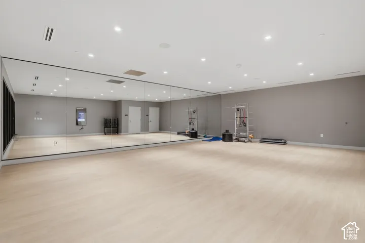 Expansive room featuring floor-to-ceiling mirrored walls, light-toned wood-finish flooring, recessed ceiling lighting, and smooth-finish neutral walls