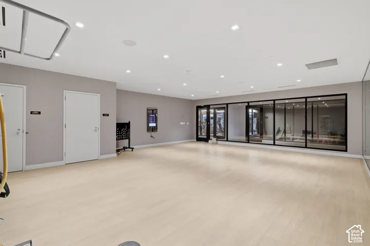 Open-concept interior featuring light wood-finish flooring, recessed lighting, large glass-paneled walls with black metal framing, and neutral wall tones
