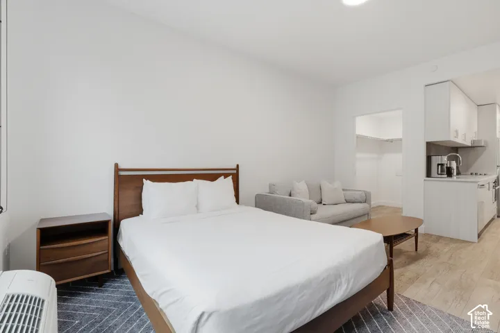 Open-concept space featuring wood-finish flooring, a walk-in closet with built-in shelving, and a kitchenette equipped with light-toned cabinetry and stainless steel appliances