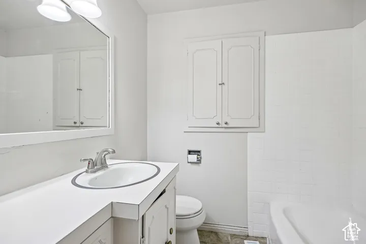 Bathroom featuring a white vanity with an integrated basin, a large wall-mounted mirror, white wall-mounted cabinetry, and a tub surround finished in white tile