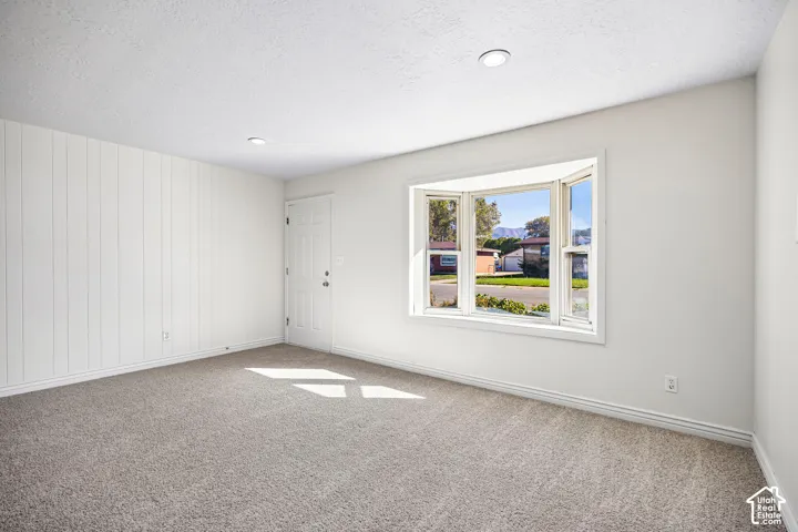 Interior room featuring a bay window, vertical panel wall accent, neutral carpeting, and recessed ceiling lighting