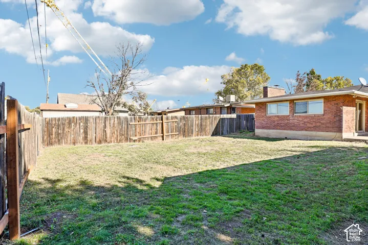 Rear exterior featuring a brick facade, chimney, fenced perimeter, and open yard space