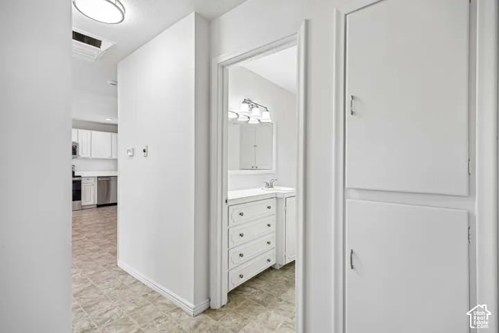 Hallway featuring full-height built-in linen cabinetry, tile flooring, and a bathroom entry with a white vanity, four-drawer storage, and wall-mounted vanity lighting