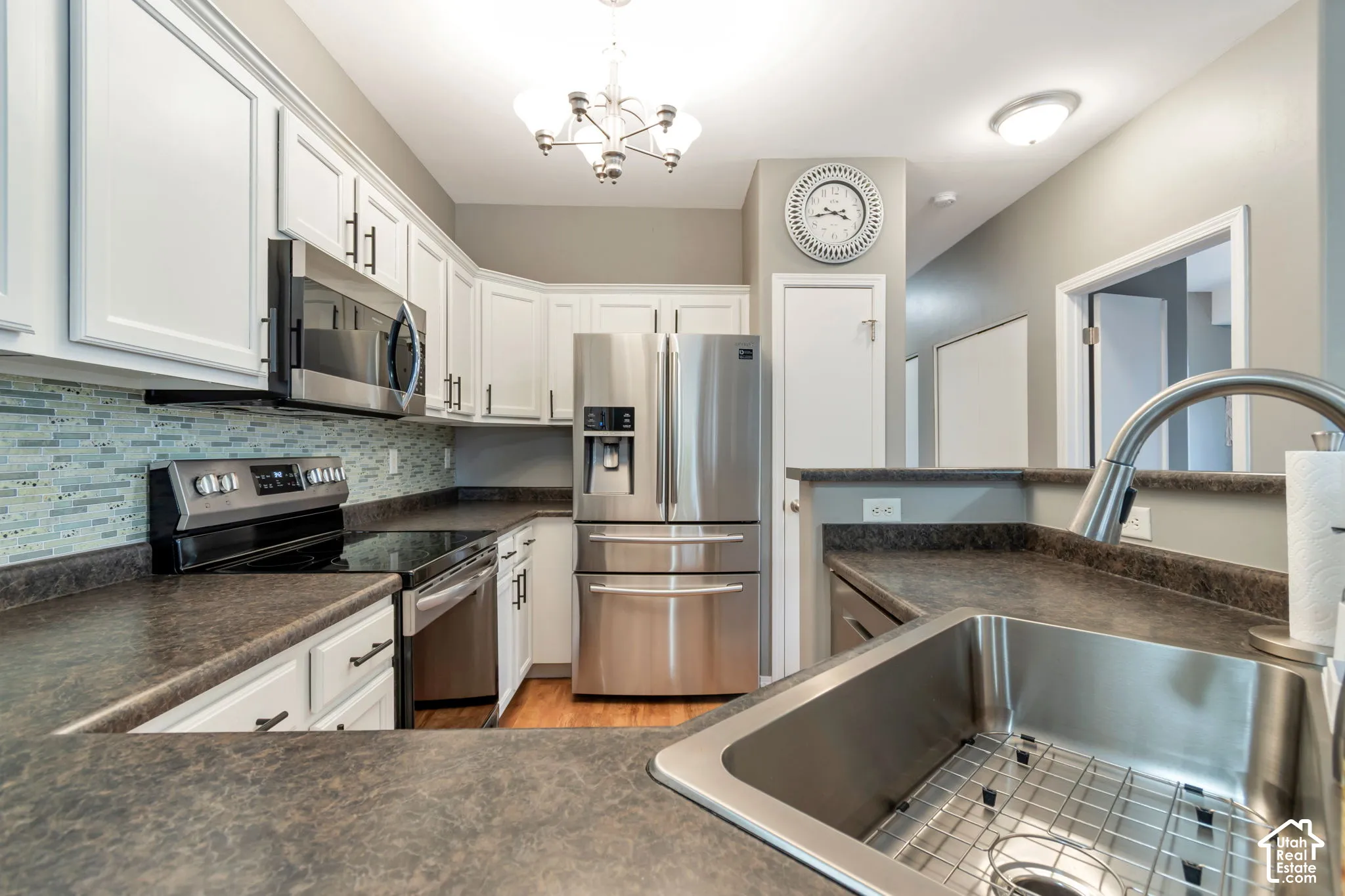 Kitchen featuring white cabinetry with dark hardware, stainless steel appliances, a multi-tonal tile backsplash, dark laminate countertops, and a stainless steel undermount sink with a gooseneck faucet