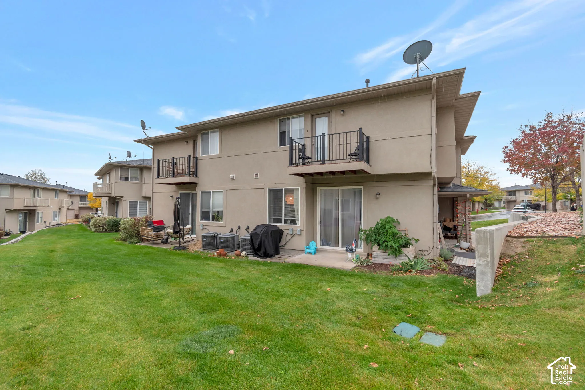 Rear exterior featuring stucco siding, two upper-level balconies with black metal railings, a concrete patio, and an expansive lawn