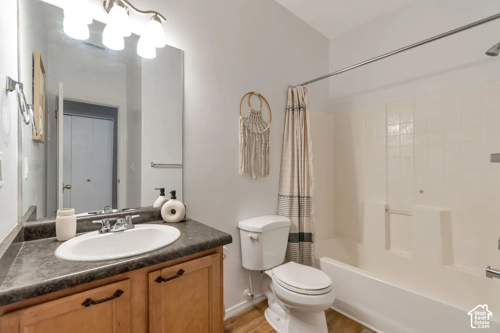 Bathroom featuring a wood-finish vanity with a molded countertop, integrated oval sink, chrome dual-handle faucet, and wall-mounted vanity lighting above a full-width mirror