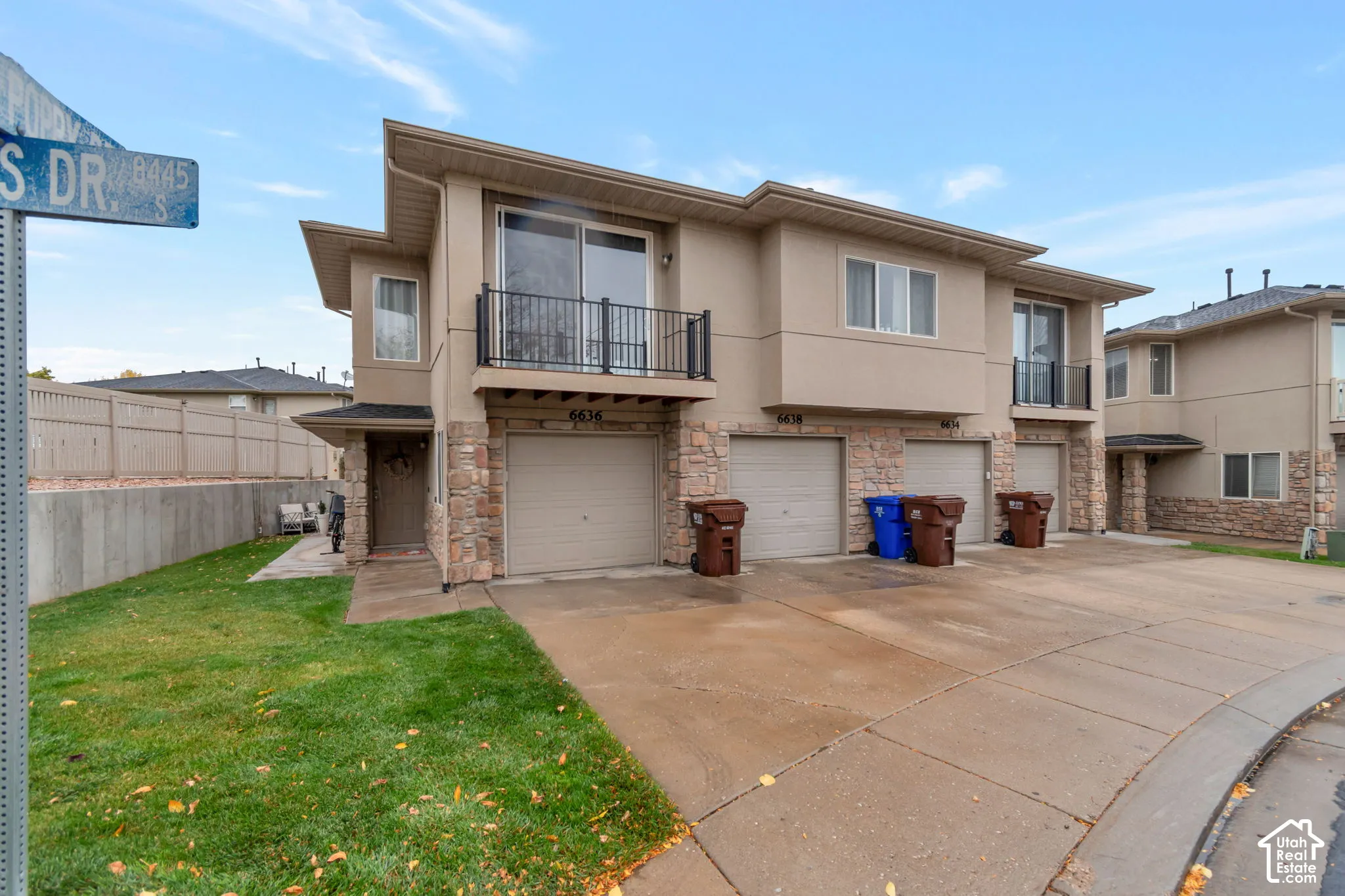 Multi-unit exterior featuring stucco and stone veneer siding, concrete driveway, attached garages, and second-story balconies with metal railings