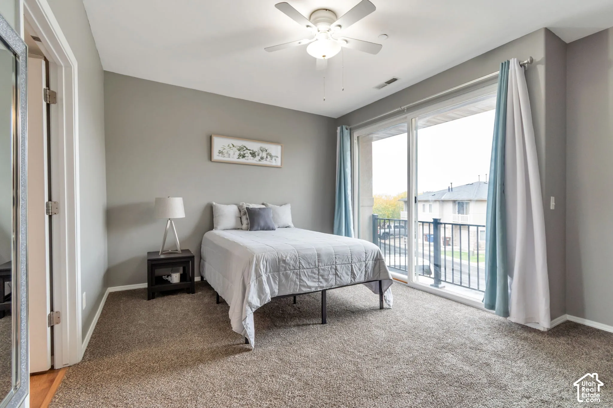 Neutral-toned interior featuring wall-to-wall carpeting, a ceiling fan with integrated lighting, and a large sliding glass door providing access to a private balcony with metal railing