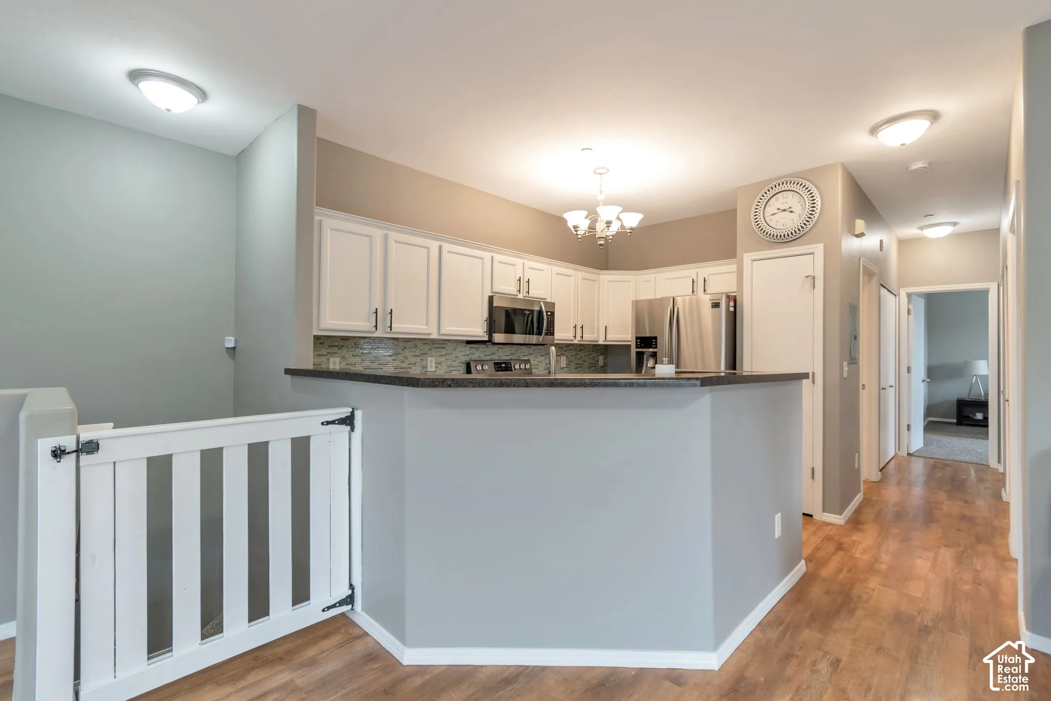 Kitchen featuring white cabinetry, dark countertops, built-in stainless steel appliances, multi-toned tile backsplash, and wood-finish flooring