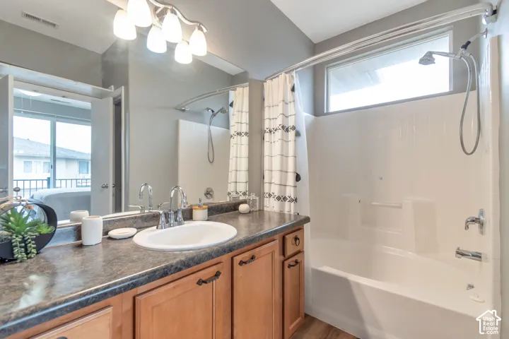 Bathroom featuring a vanity with wood-finish cabinetry, a dark-toned solid-surface countertop, an integrated oval sink, a wall-to-wall mirror, and a tub-shower combination with a transom window