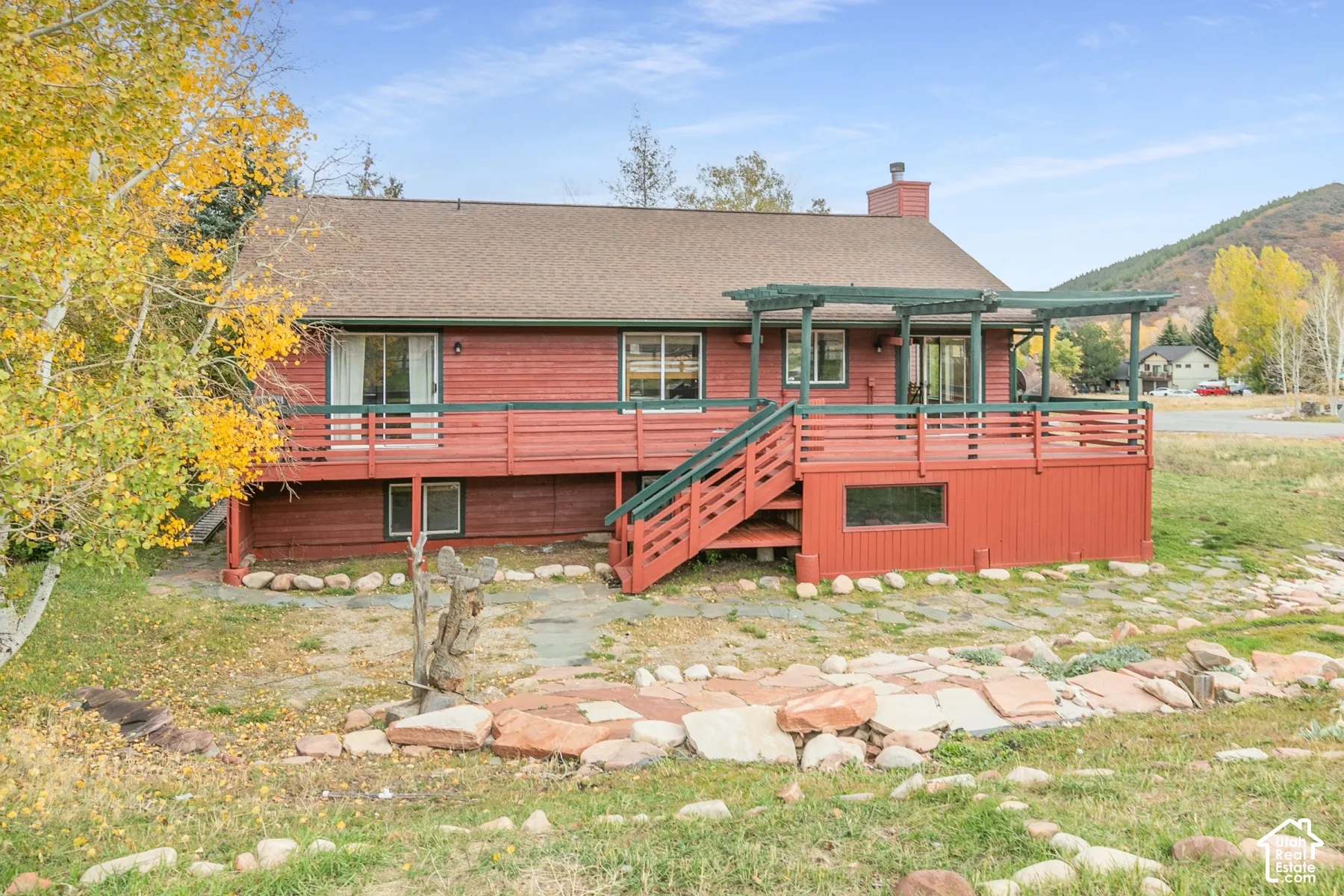 Red wood-sided exterior featuring an elevated deck with a pergola, staircase, and stone-accented landscape