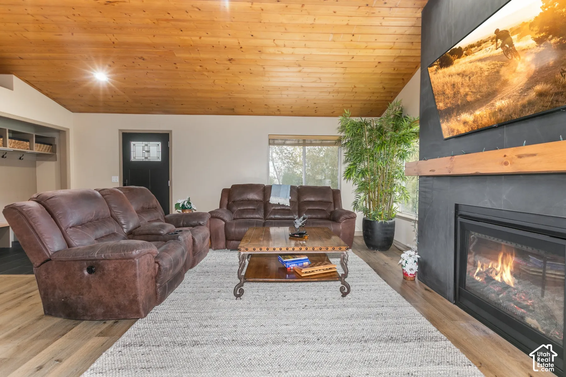 Vaulted wood-paneled ceiling, fireplace with floor-to-ceiling matte surround, natural wood mantel, and wood-finish flooring