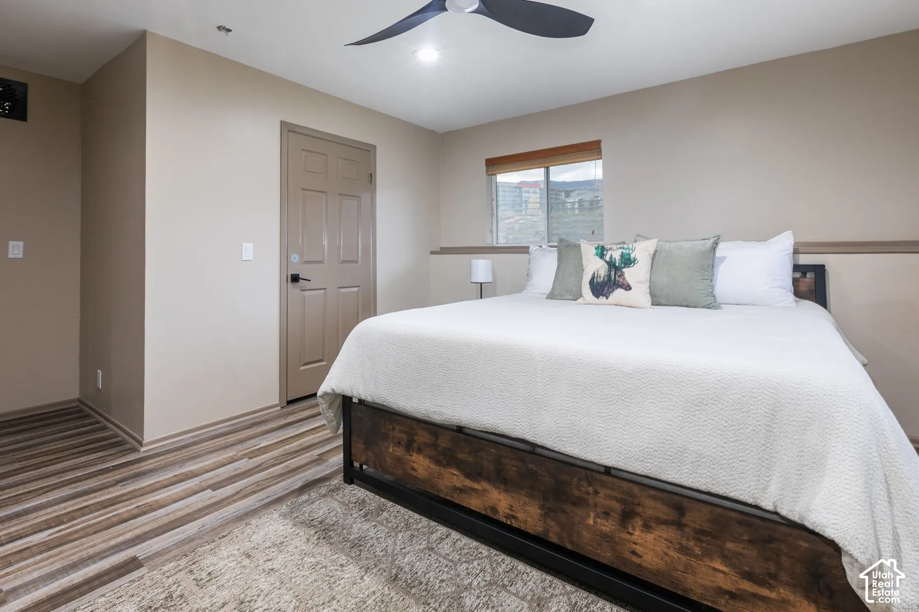 Room featuring wood-finish flooring, a multi-blade ceiling fan, neutral wall paint, a six-panel door, and a horizontal sliding window