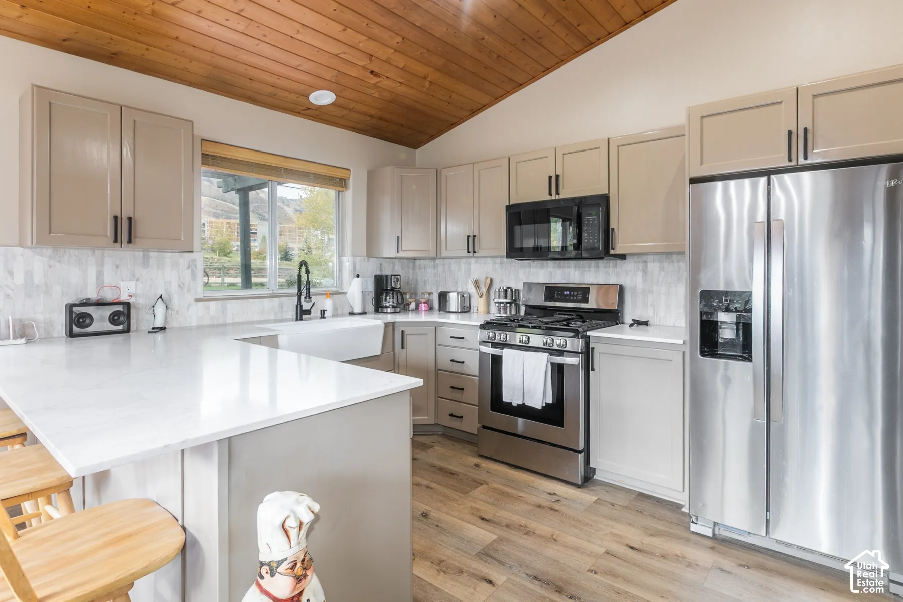 Kitchen featuring wood-paneled vaulted ceilings, shaker-style cabinetry, quartz countertops, white farmhouse-style sink, and stainless steel appliances