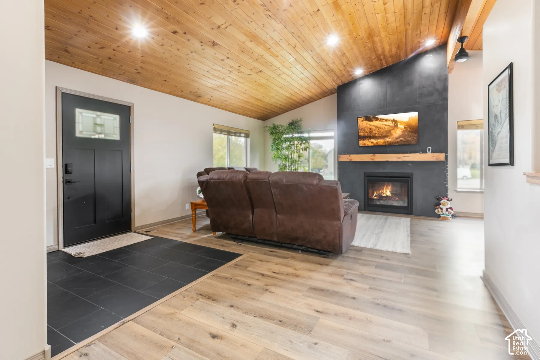 Vaulted ceiling with wood-plank finish, dark stone-finish fireplace surround with a natural wood mantel, recessed lighting, wood-finish flooring, and slate-finish tile entryway