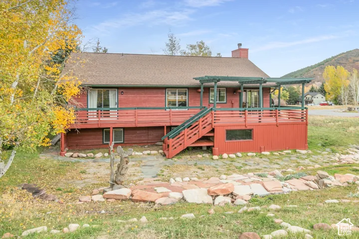 Red wood-sided exterior featuring an elevated deck with a pergola, staircase, and stone-accented landscape