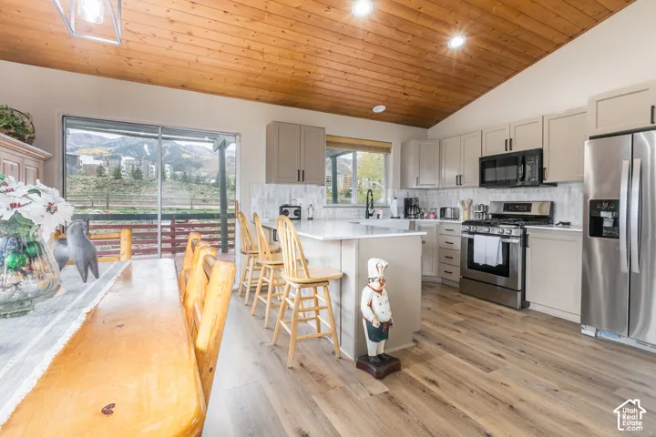 Vaulted wood-paneled ceiling, light-toned cabinetry, quartz countertops, stainless steel appliances, and wood-finish flooring