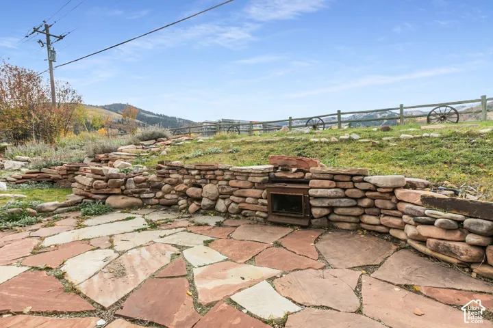Flagstone patio featuring a natural stone retaining wall with an integrated metal firebox, terraced landscaping, and a post-and-rail fence
