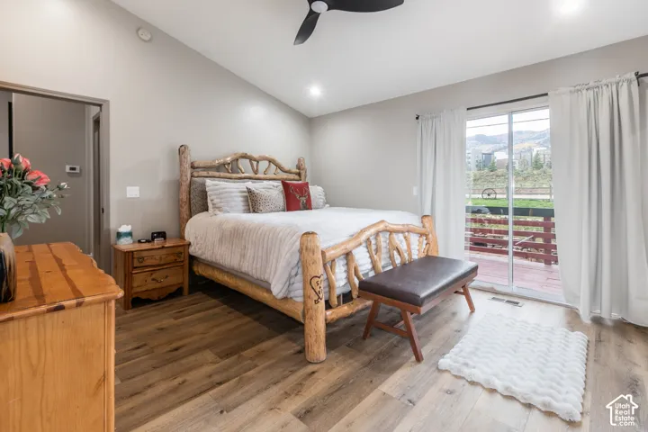 Vaulted ceiling featuring a matte black finish ceiling fan, wood-finish flooring, and sliding glass doors with access to an exterior deck