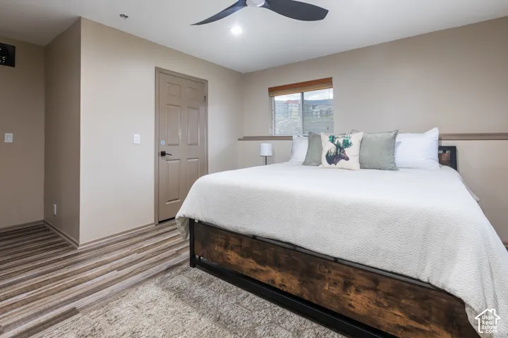 Room featuring wood-finish flooring, a multi-blade ceiling fan, neutral wall paint, a six-panel door, and a horizontal sliding window