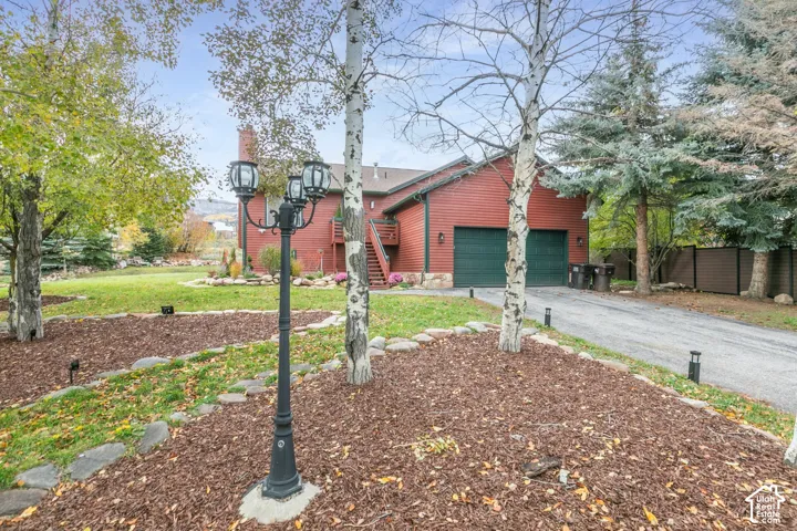Red lap siding exterior featuring a two-car garage, stone-lined landscaping beds, mature trees, and a decorative metal light post