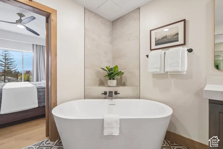 Freestanding soaking tub featuring matte black wall-mounted fixtures, full-height stone-finish tile surround, integrated corner shelving, and decorative patterned floor tiling