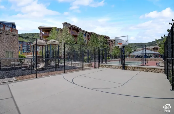 Fenced recreational area featuring a paved basketball court, tennis court, and playground equipment